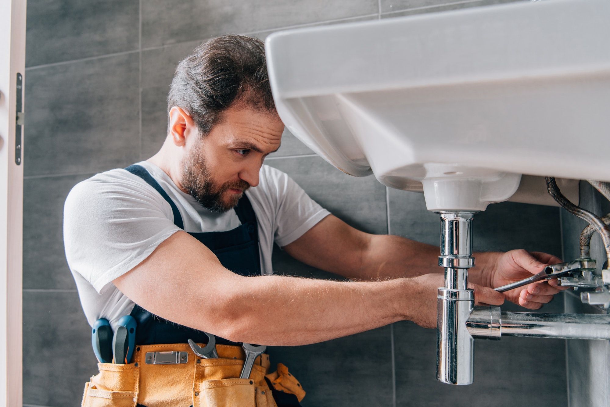 Sanitärtechniker repariert Leitungen unter einem Waschbecken im Badezimmer
